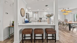 A modern kitchen with white cabinetry, a central island with stools, and pendant lighting. - Blue Yonder Beach House (New Smyrna Beach)