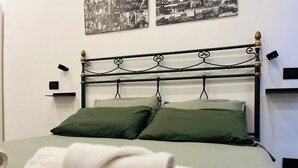 A bed with a metal frame and two pillows, a wall-mounted shelf, and a towel rack with towels. - Stylish&Renovated Apt in Trastevere ac/wi-fi (Roma)
