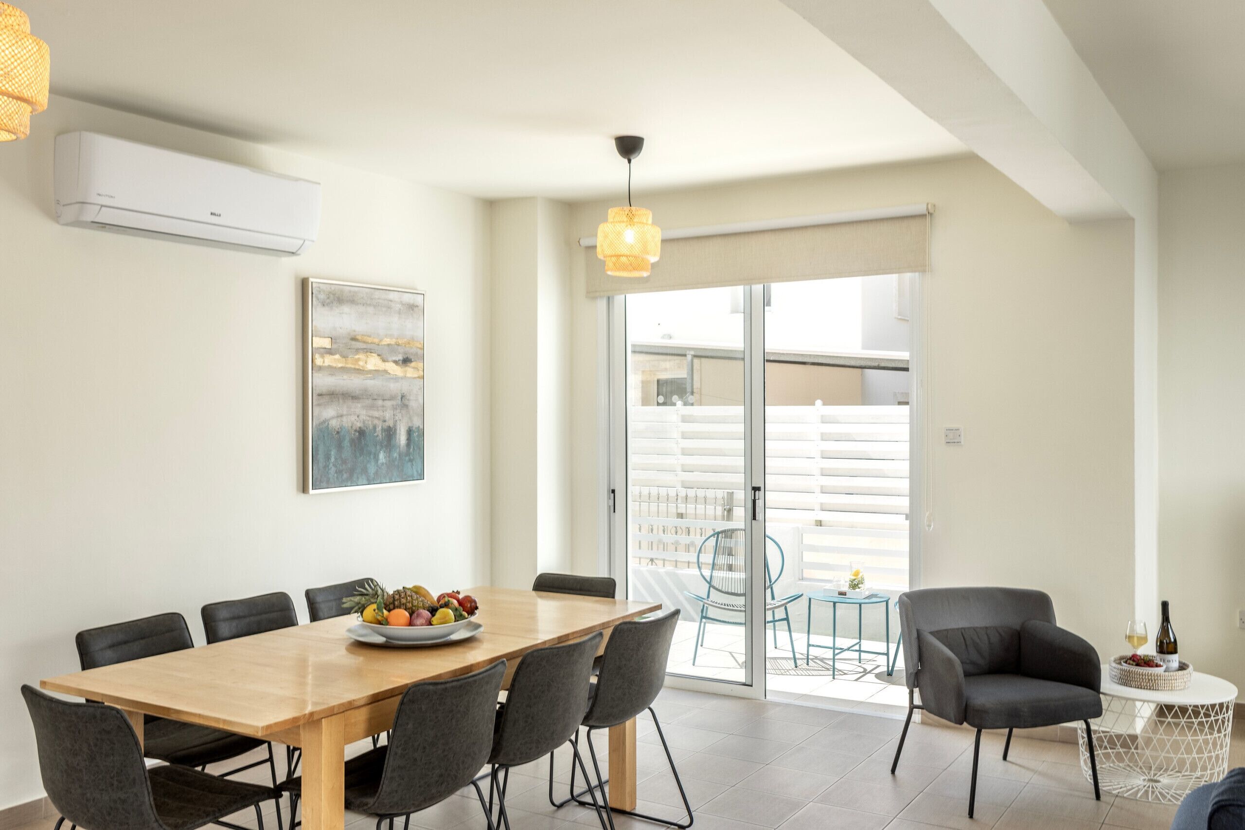 A dining area with a wooden table and chairs, a fruit bowl, and a view of the outside.