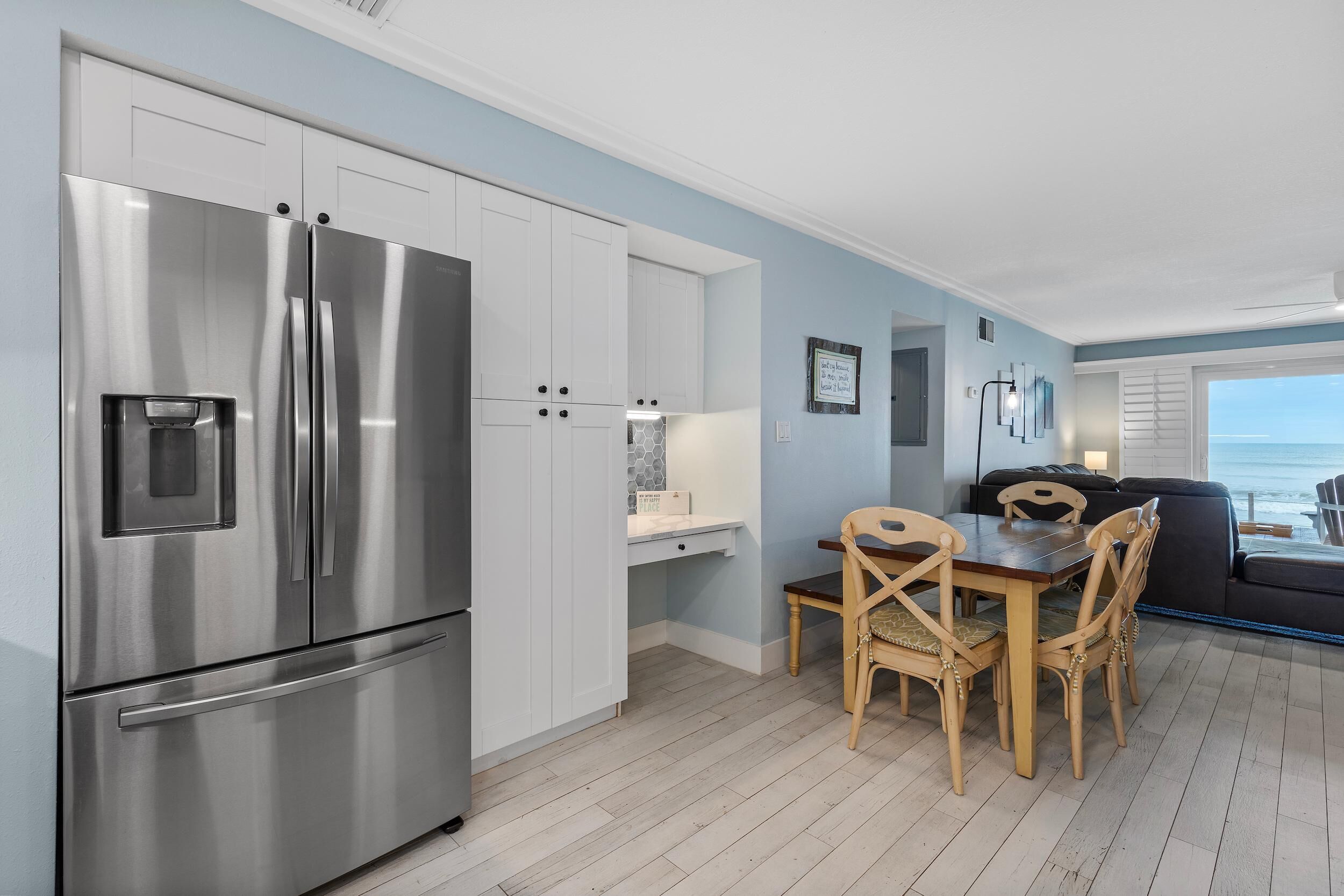 Una cocina moderna con un refrigerador de acero inoxidable, armarios blancos y un comedor con sillas y mesa de madera.