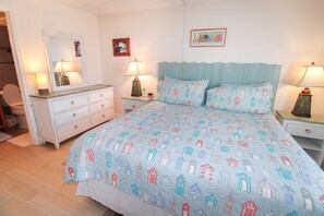Une chambre à coucher comprenant un lit, une commode, un miroir, deux tables de chevet avec des lampes et un mur orné d’un tableau encadré.