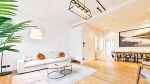 A modern living room with a white sofa, round coffee table, and a dining area with a wooden table and chairs. - Wonderful Fitzrovia 3 Bed Apartment (Greater London)