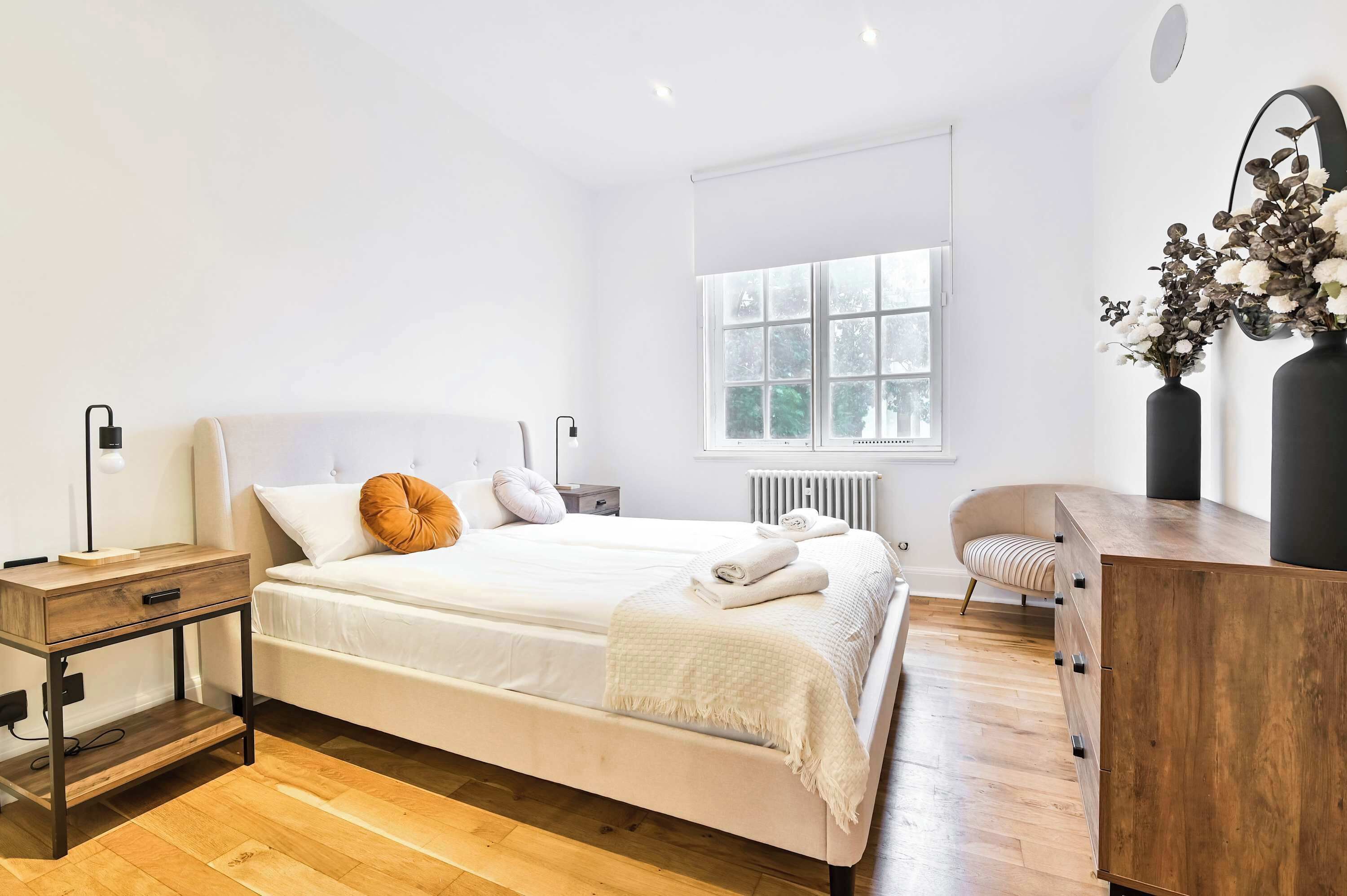 Een moderne slaapkamer met een bed, nachtkastjes, een stoel en een dressoir.