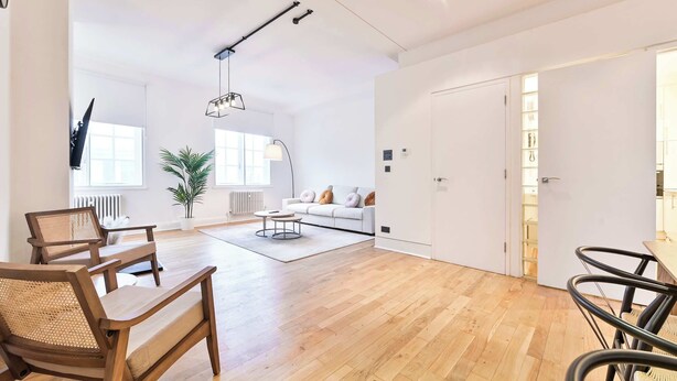 A spacious living area with a wooden floor, a sofa set, and a dining table with chairs. - Wonderful Fitzrovia 3 Bed Apartment (Greater London)