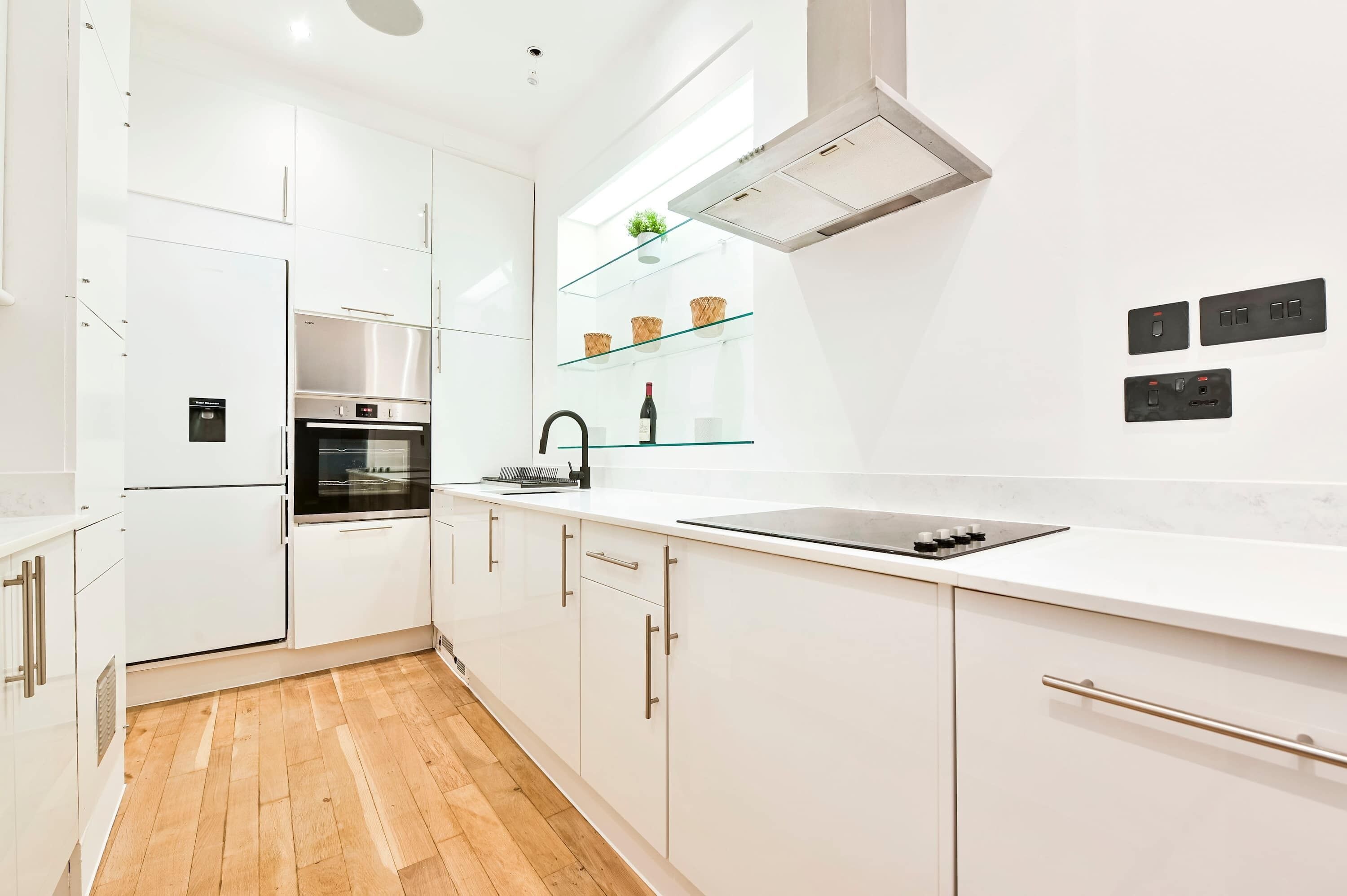 A modern kitchen with white cabinetry, a stainless steel oven, a built-in stove, and a glass shelf with baskets.
