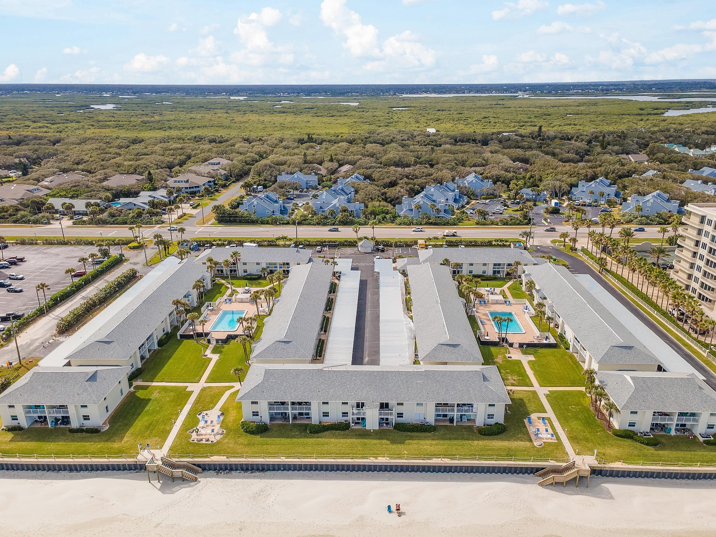 A large resort with multiple buildings, a central pool, and a beach area.