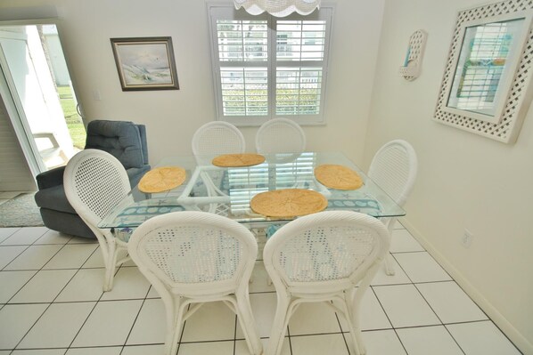 Un coin repas avec une table en verre, des chaises en osier blanc et une vue par la fenêtre.