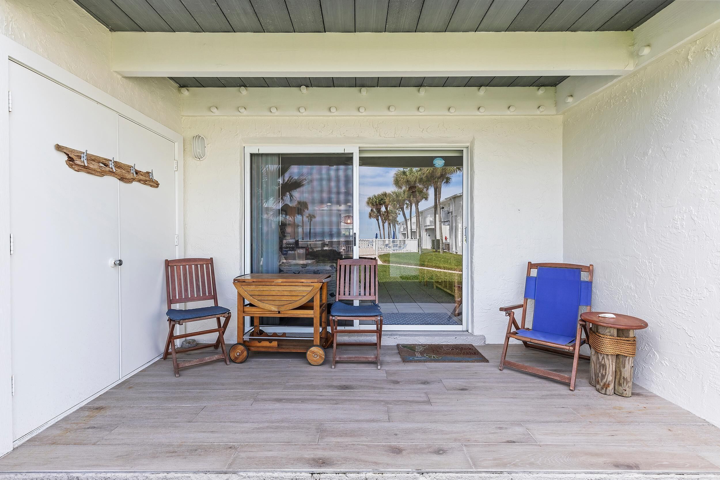 A covered outdoor seating area with a table and two chairs, a wooden bench, and a small round table with a woven base.