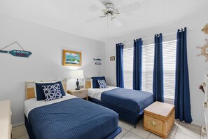 A room with two beds, a ceiling fan, a framed picture, and a window with curtains. - Colony Beach Club 139 (New Smyrna Beach)
