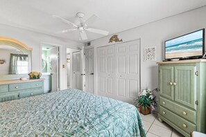 Une chambre à coucher avec un lit, un ventilateur de plafond, un téléviseur et une armoire verte.
