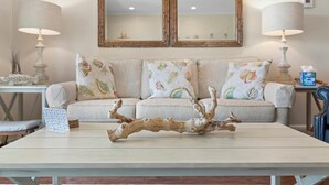 A living room with a sofa, two lamps, a coffee table with a decorative branch, and a mirror above the sofa.