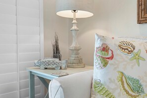 A room with a white lamp, a small table with decorative items, and a cushion with a sea-themed pattern. - Colony Beach Club 204 (New Smyrna Beach)