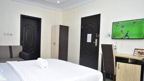 A hotel room with a bed, a desk, a chair, and a TV displaying a soccer game. - Ai-Royal Hotel & Suites (Ikorodu)