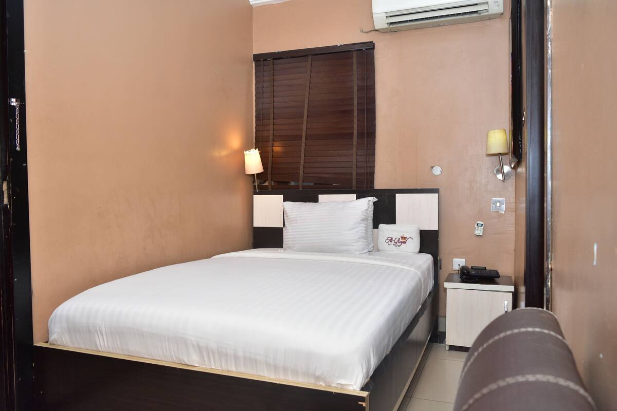 Una habitación de hotel con una cama individual, una mesita de noche con lámpara y un pequeño armario.