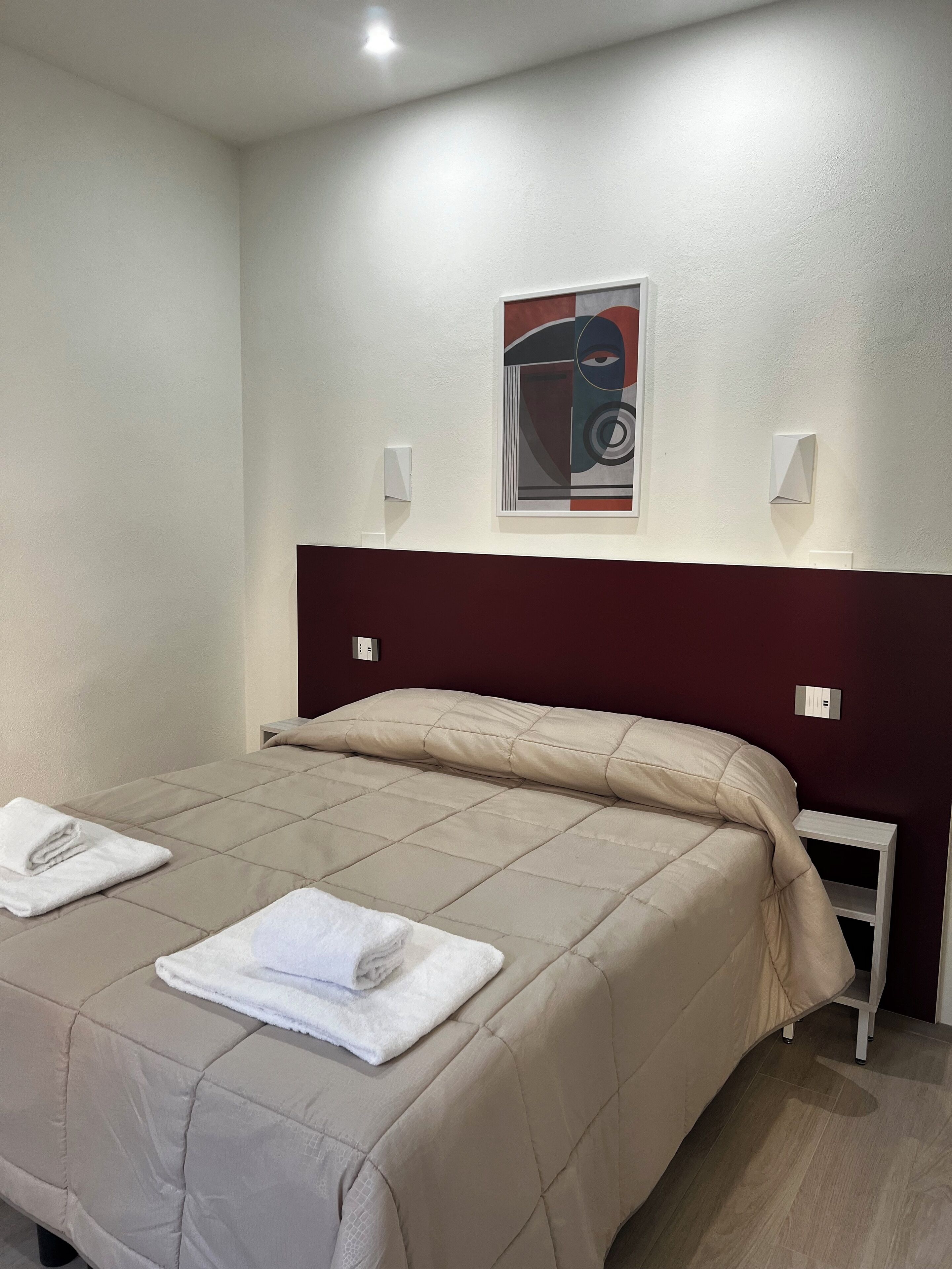 A hotel room with a bed, a headboard, a wall-mounted artwork, and a nightstand.