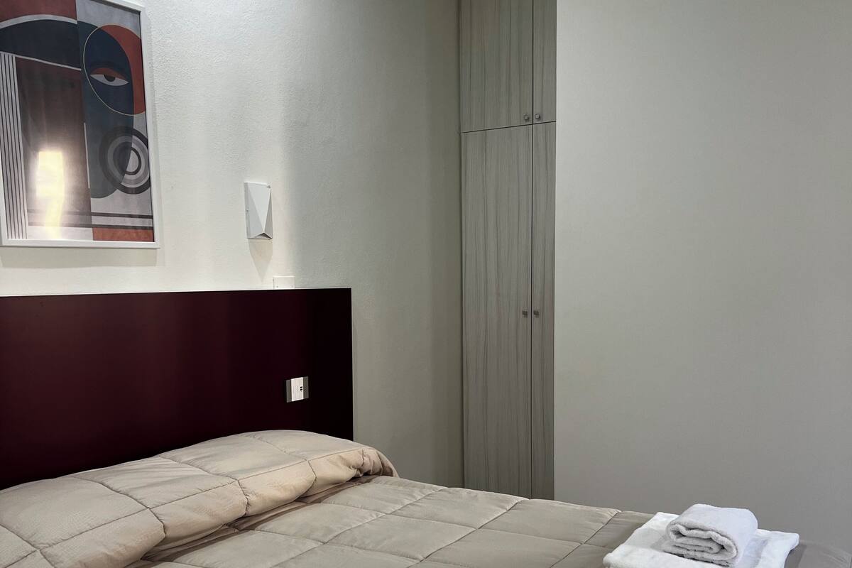 A hotel room with a bed, a wardrobe, and a wall-mounted light.