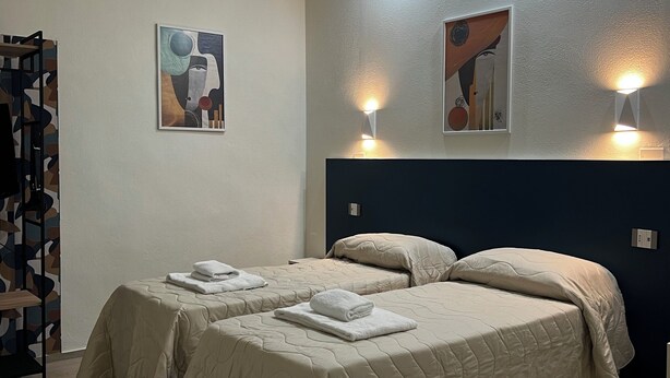 A hotel room with two beds, a large painting on the wall, and a wooden floor. - Bella Ciao Firenze (Florence)