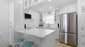 A modern kitchen with white cabinetry, a stainless steel refrigerator, and a central island with bar stools. - Colony Beach Club 220 (New Smyrna Beach)