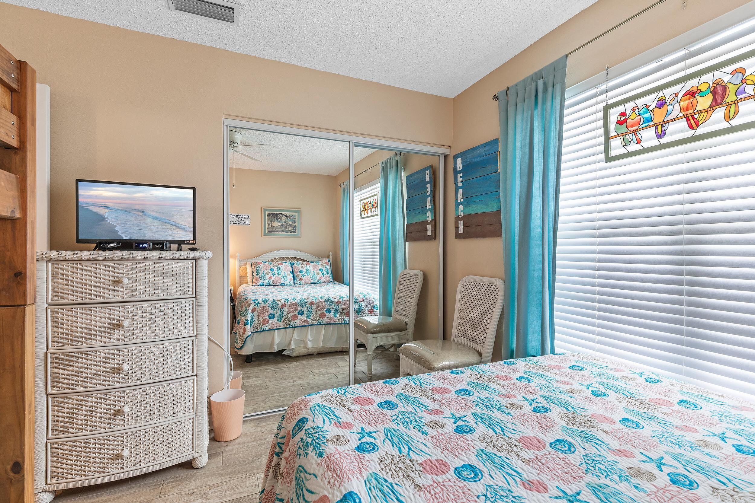 A bedroom with a bed, a dresser, a chair, a television, and a window with blinds.