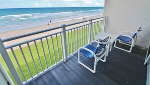 A balcony with two blue and white cushioned chairs, a small table, and a view of the beach and ocean. - Colony Beach Club 223 (New Smyrna Beach)