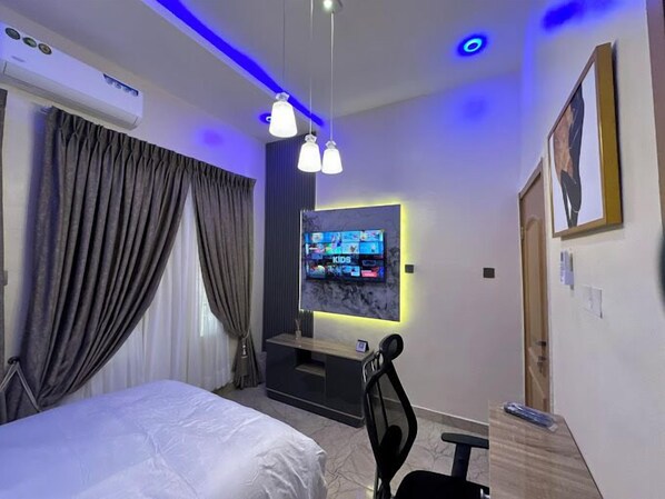 A modern hotel room with a large bed, a TV mounted on the wall, and a desk with a chair.