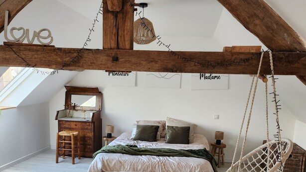 Een slaapkamer met een bed, een hangstoel, een houten dressoir en een dakraam.