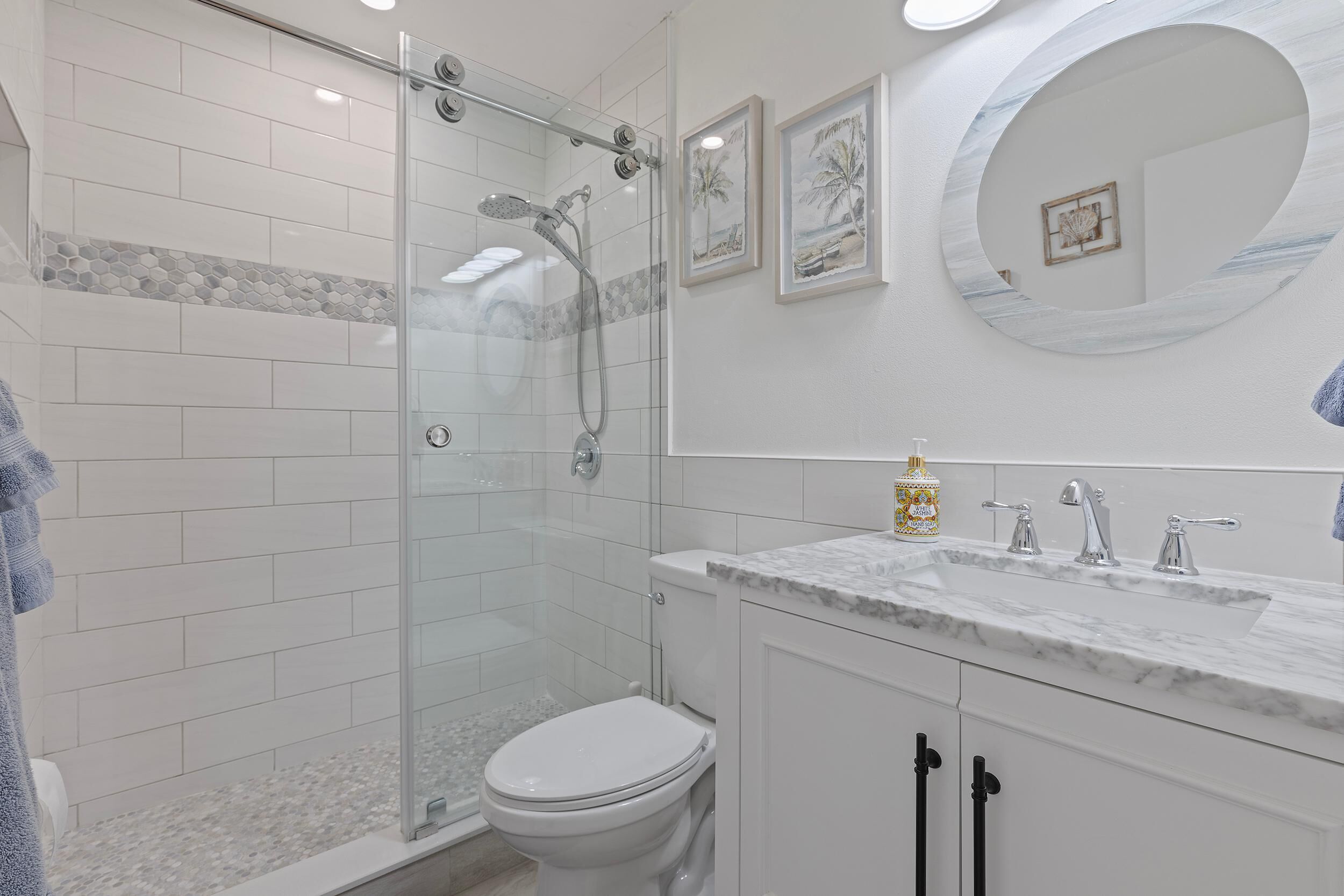 A modern bathroom with a glass-enclosed shower, white tiles, a marble sink, and a toilet.