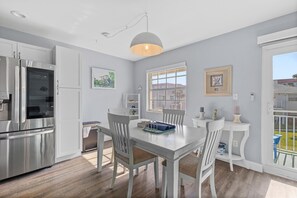 A modern kitchen with white cabinetry, stainless steel appliances, and a dining area with a white table and chairs. - Colony Beach Club 237 (New Smyrna Beach)