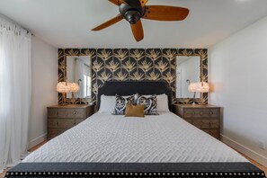 Een slaapkamer met een groot bed, twee nachtkastjes, een plafondventilator en twee spiegels aan de muur.
