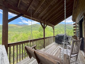 A wooden deck with a swing chair, a covered grill area, and a view of green hills. - Sleepy Bear Log Cabin with View, WiFI (Maggie Valley)