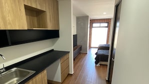 A modern kitchen with wooden cabinets and a black countertop, leading to a bedroom with a bed and a window.