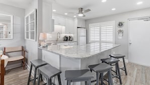 A kitchen with a large island, bar stools, a ceiling fan, and a refrigerator.