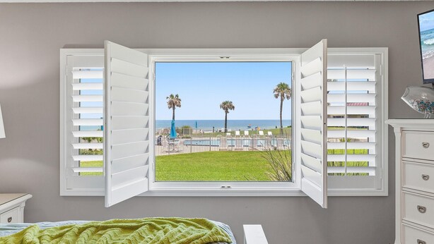 A bedroom with a large window, a bed, and a dresser.