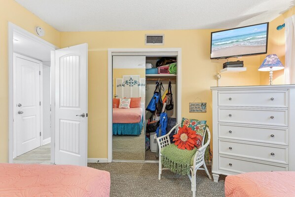 A bedroom with a bed, a dresser, a chair, a TV, and a closet. - Chateau by the Sea 13C (New Smyrna Beach)