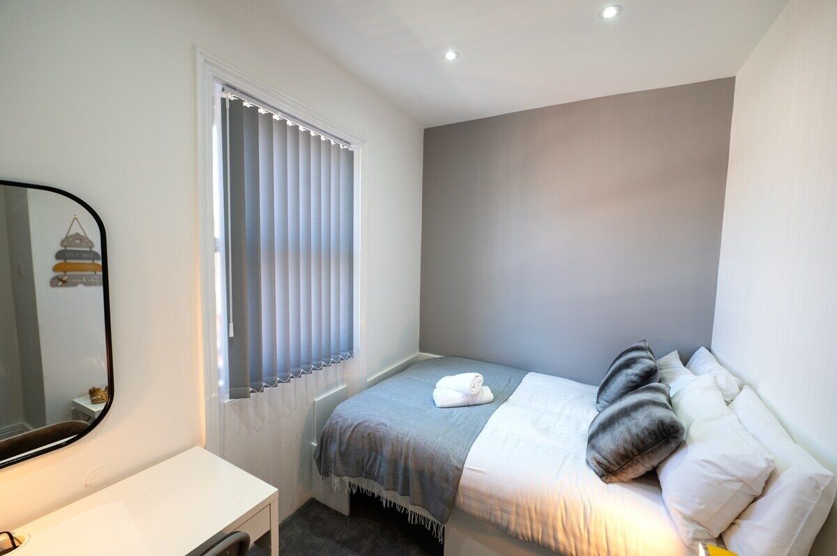 A bedroom with a bed, a bedside table, and a window with blinds.