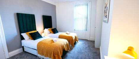Ein Hotelzimmer mit zwei Betten, einem Schreibtisch, einem Stuhl und einem Fenster mit Jalousien.
