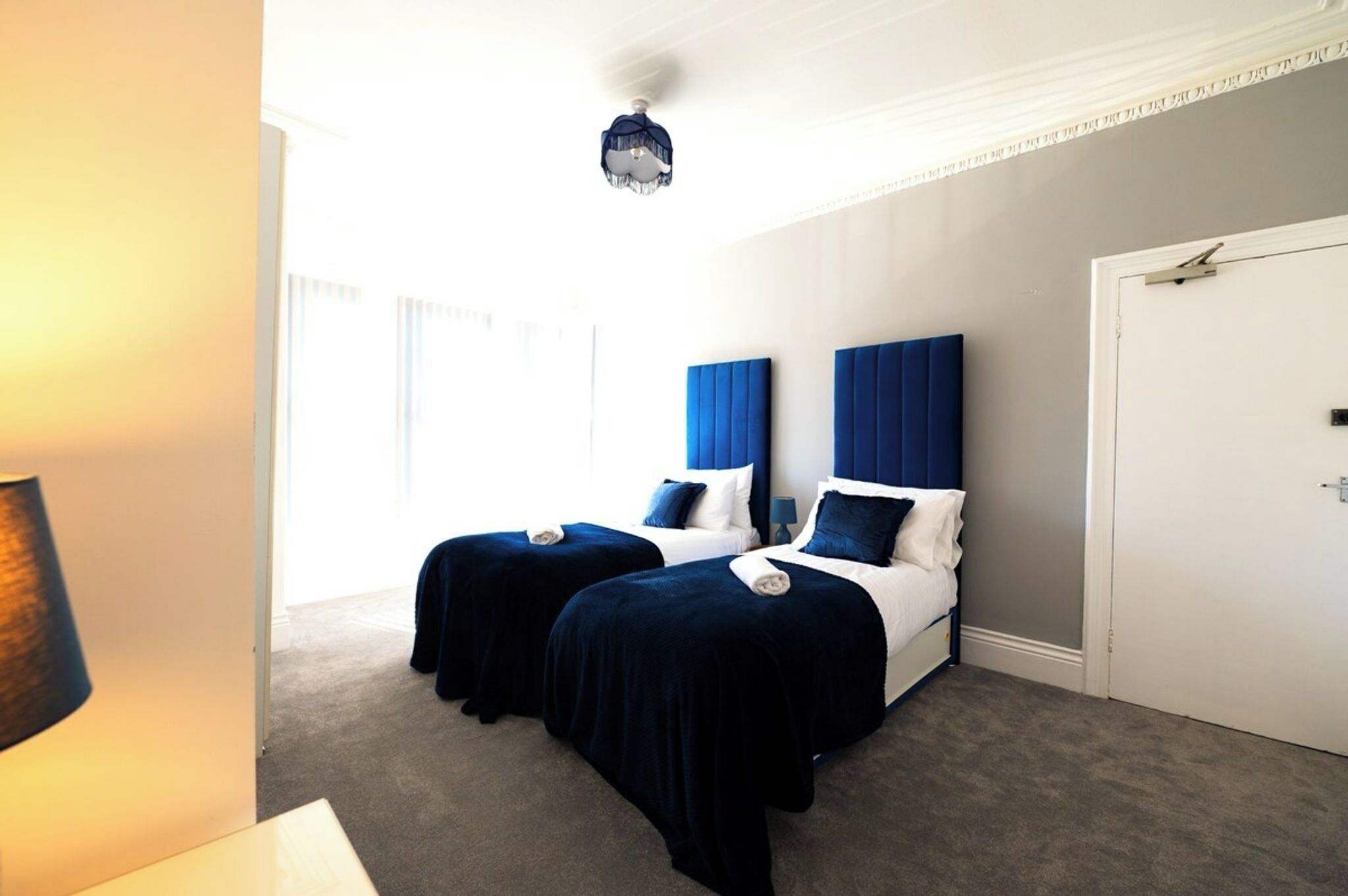 Habitación de hotel con dos camas, una puerta blanca y una lámpara en el techo.