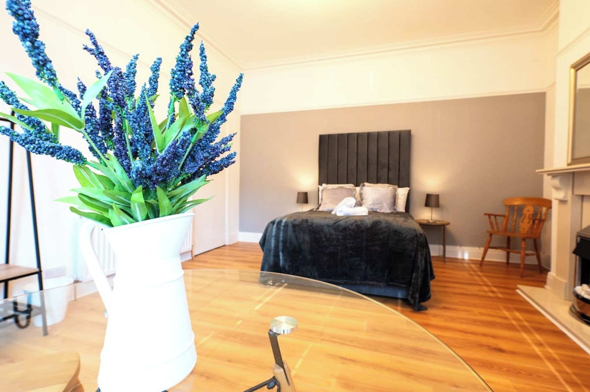 A bedroom with a bed, bedside tables, a mirror, a potted plant, and a fireplace.