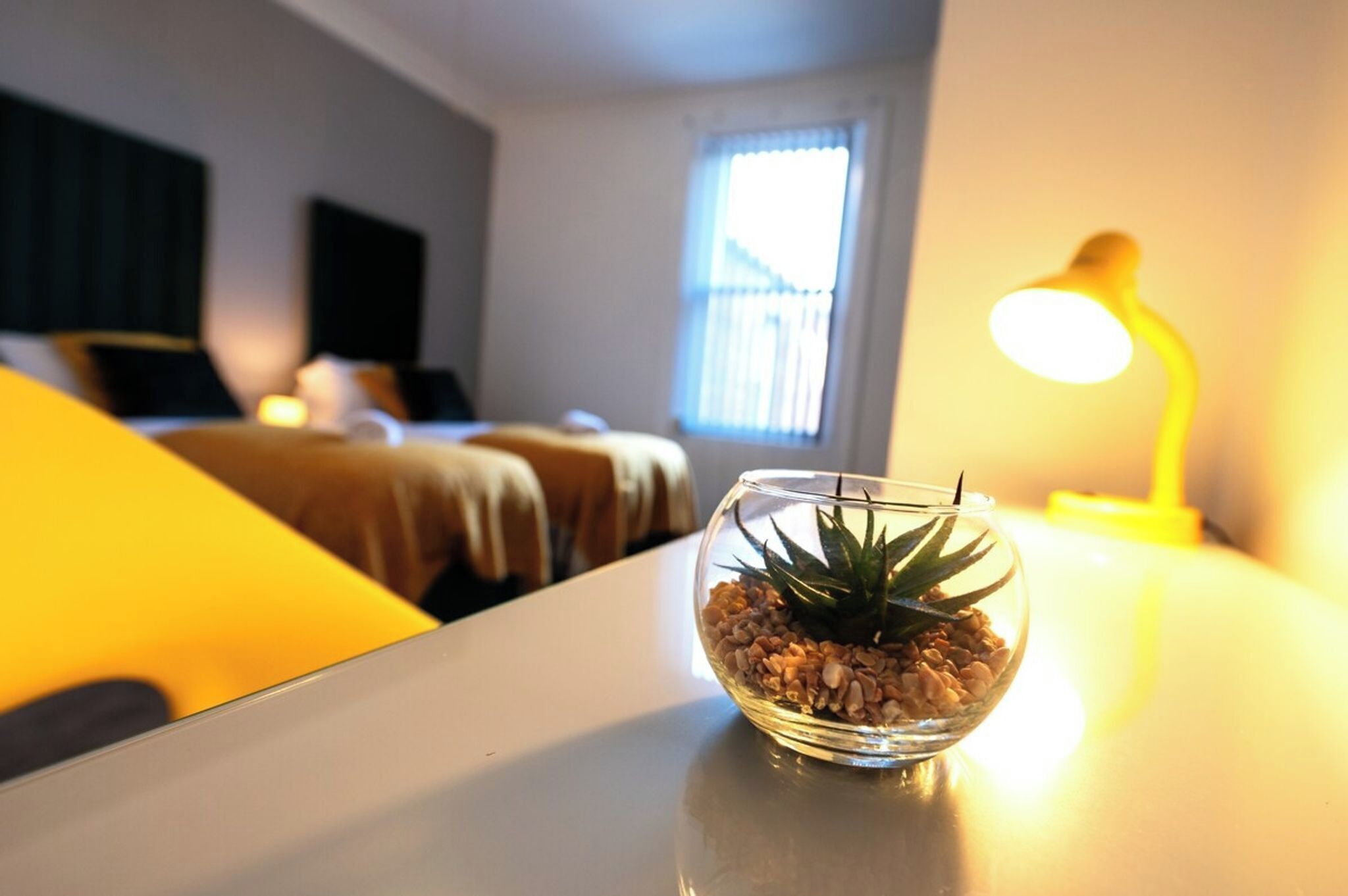 Una habitació amb un llit, una tauleta de nit amb una làmpada i una finestra amb persianes.