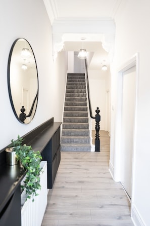A staircase with a grey carpet, a black balustrade, and a white wall with a large mirror.