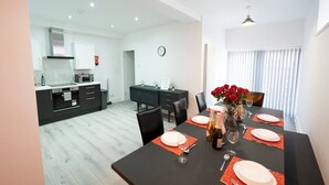 A modern dining area with a black table set for four, a vase of red flowers, and a kitchen in the background. - Lush 5-Bed Home @ Newcastle upon Tyne 
Central | Free parking | Bus @ door step (Newcastle upon Tyne)