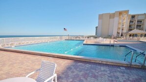 A swimming pool with a flag, lounge chairs, and a tiled deck. - Castle Reef 312 (New Smyrna Beach)