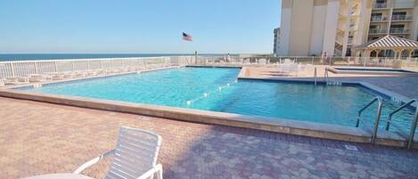 A swimming pool with a flag, lounge chairs, and a tiled deck.