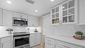 A modern kitchen with white cabinetry, stainless steel appliances, and a window with glass doors. - Castle Reef 312 (New Smyrna Beach)