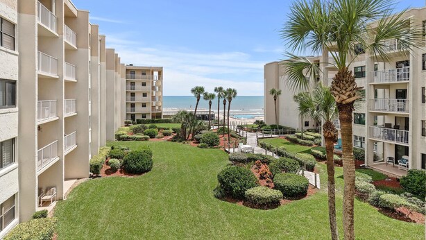 A hotel courtyard with a pool, palm trees, and a view of the ocean. - Castle Reef 312 (New Smyrna Beach)
