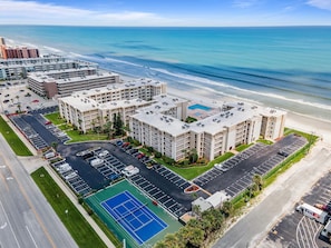 A high-rise hotel with multiple floors, a parking lot, and a tennis court. - Castle Reef 314 (New Smyrna Beach)