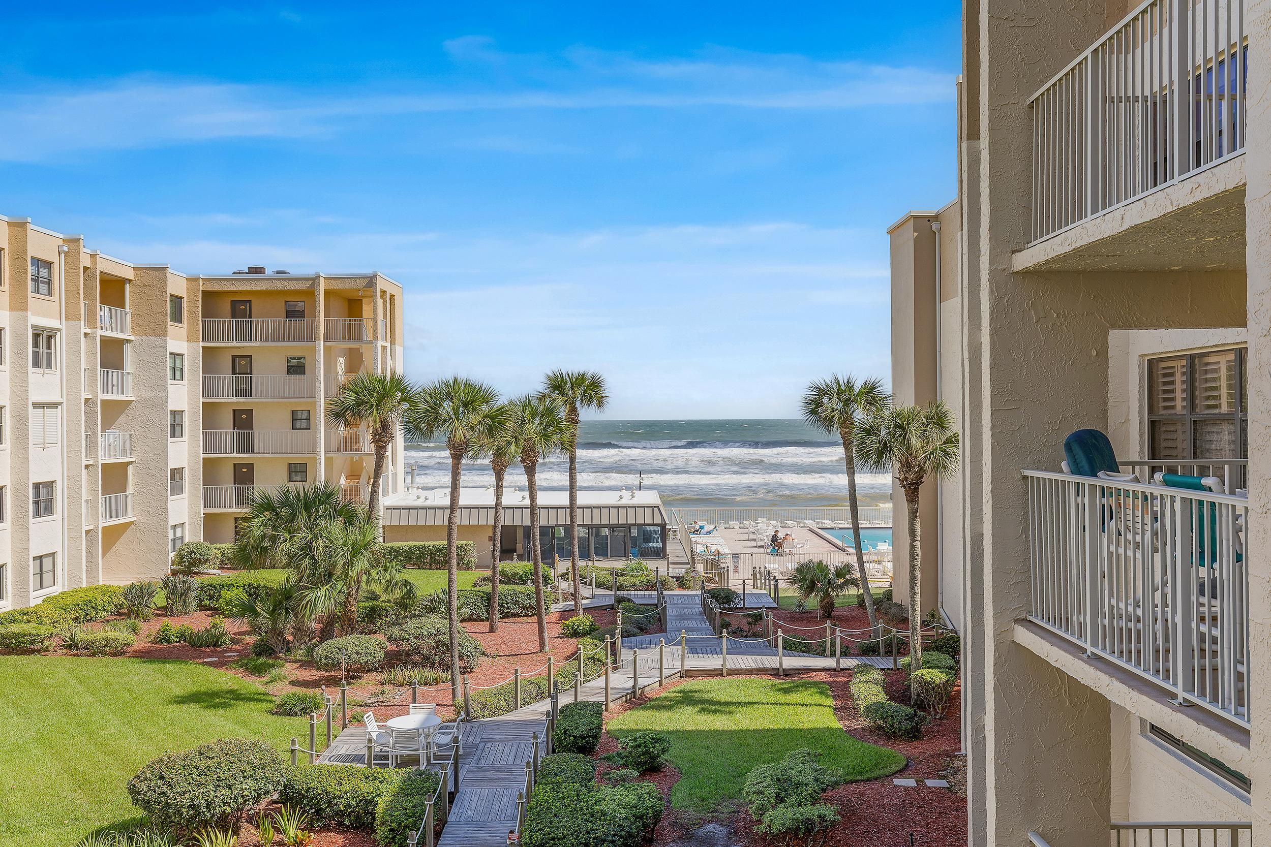 A beachfront hotel with multiple balconies, a pool area, and a view of the ocean.