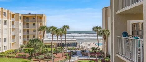 A beachfront hotel with multiple balconies, a pool area, and a view of the ocean.