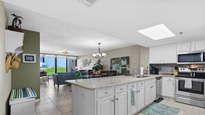 A modern kitchen with white cabinetry, a large island, stainless steel appliances, and a view to the outdoors. - Chadham by the Sea 118 (New Smyrna Beach)