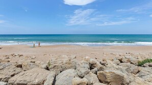 A rocky beach with clear blue water and a few people in the distance. - Chadham by the Sea 118 (New Smyrna Beach)